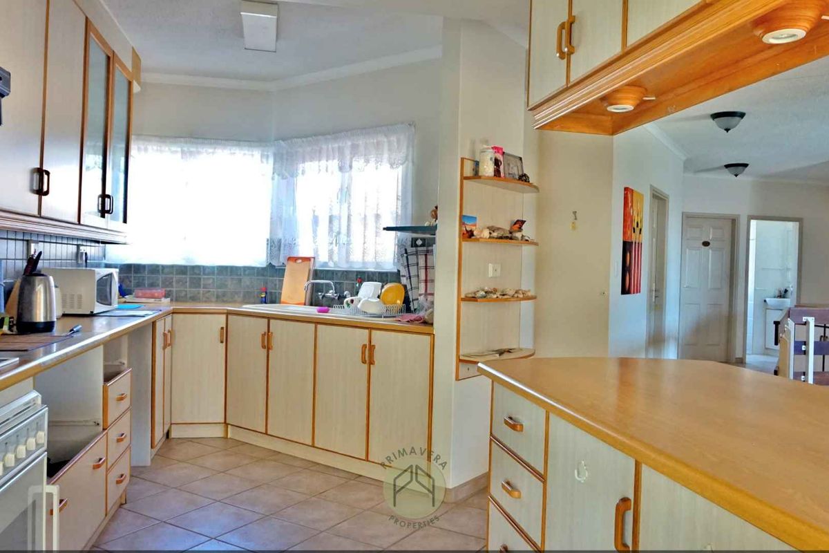 A functional kitchen featuring light-toned cabinetry, tiled splashbacks, and a breakfast bar, with an open-plan layout connecting to the adjacent living area.