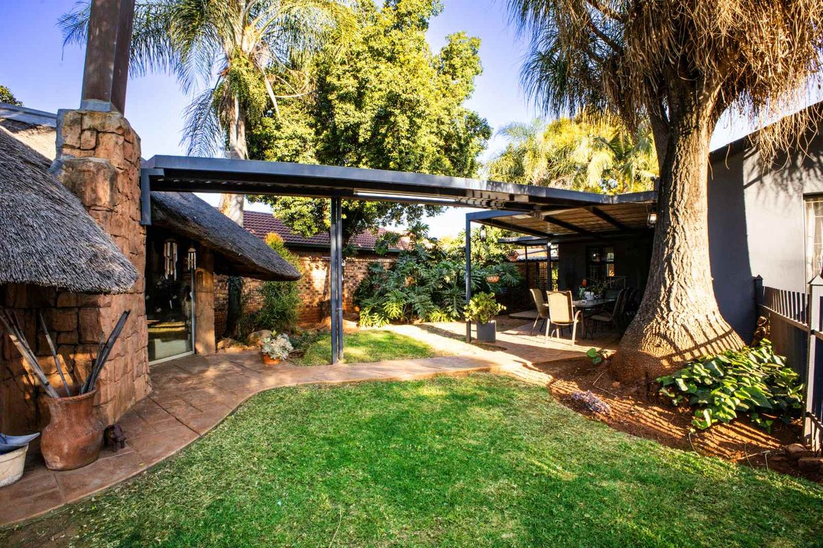 A well-maintained rear garden featuring a covered patio area, stone chimney, and a thatched roof section, providing a pleasant outdoor living space.