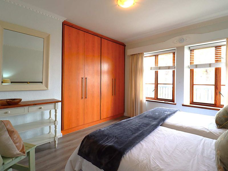 A well-maintained bedroom featuring built-in wooden wardrobes, laminate flooring, crown molding, and large windows that provide ample natural light.
