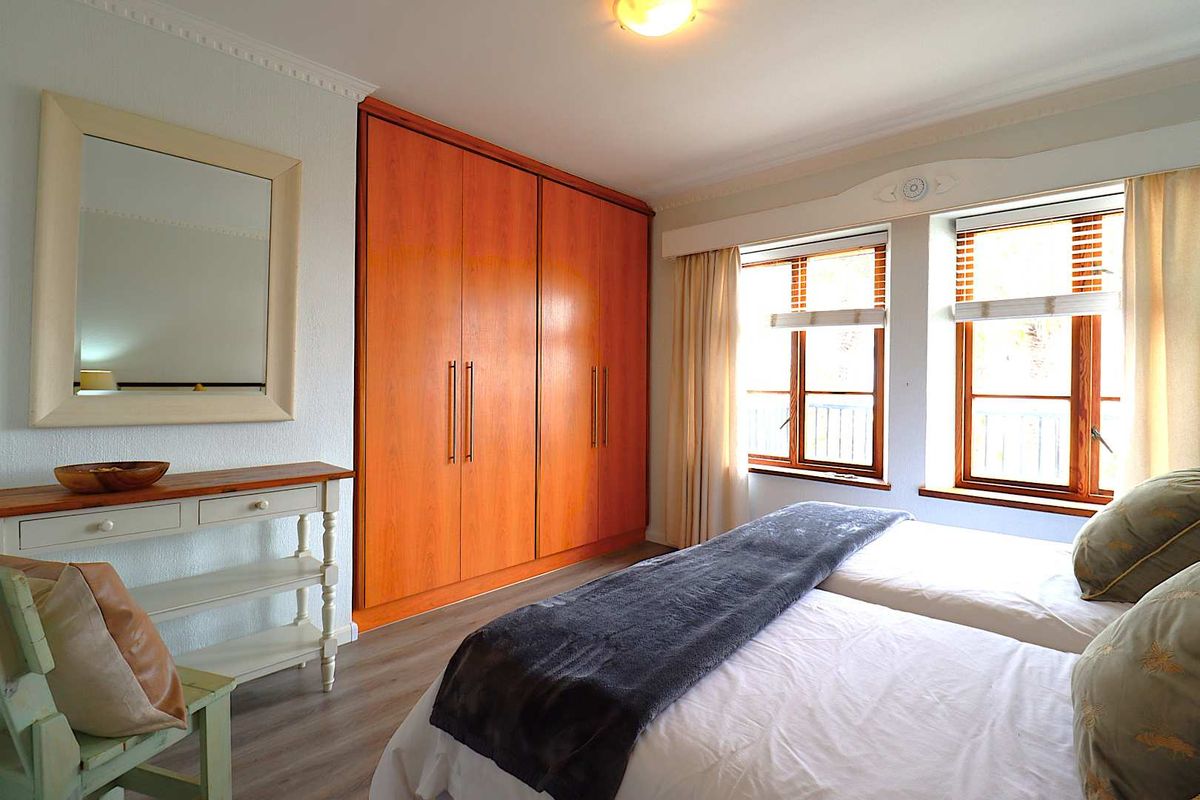 A well-maintained bedroom featuring built-in wooden wardrobes, laminate flooring, crown molding, and large windows that provide ample natural light.