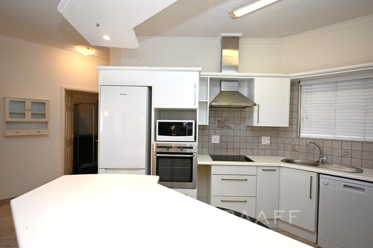 A functional kitchen featuring white cabinetry, built-in oven and microwave, stainless steel extractor fan, and tiled backsplash with a breakfast counter.