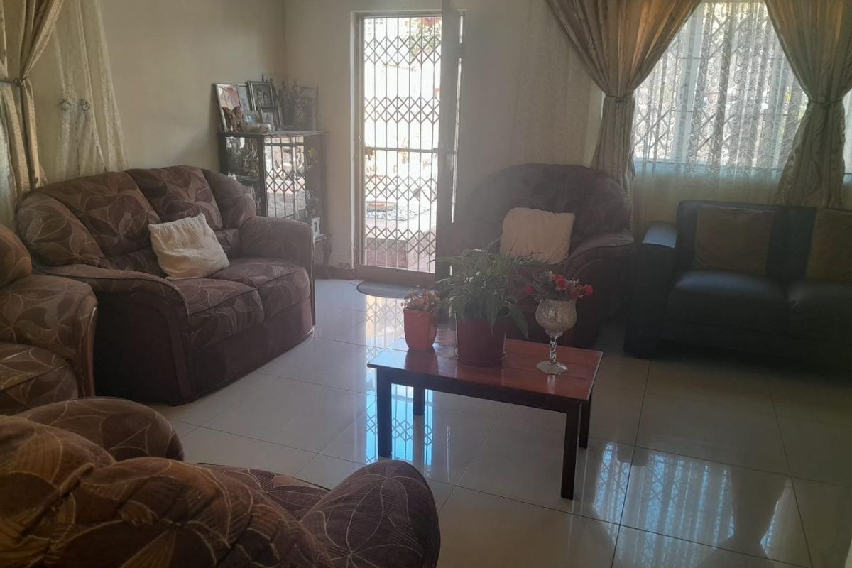 A comfortable living room featuring tiled flooring, a wall-mounted air conditioning unit, and a security gate leading to the exterior.