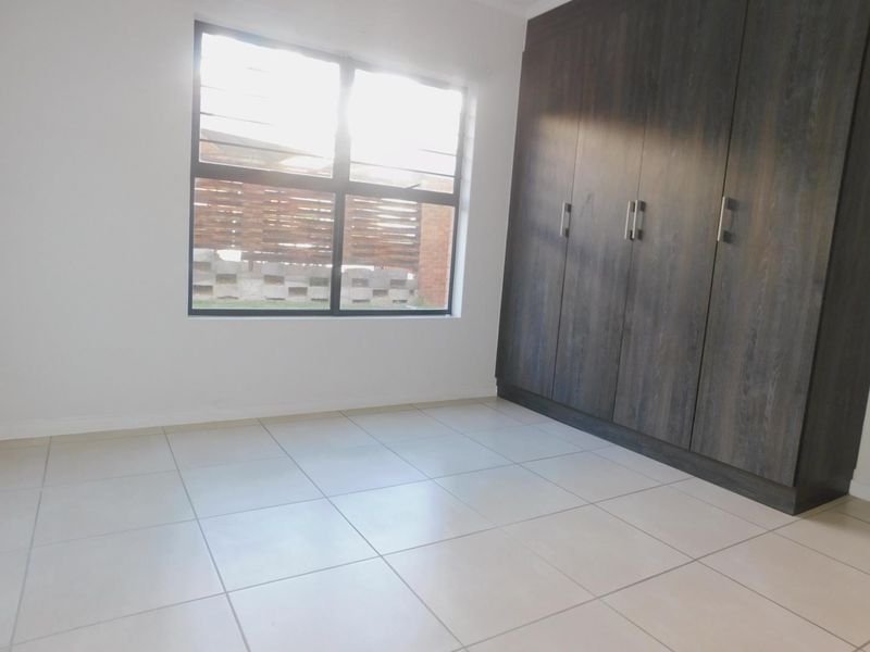 A bright, empty bedroom featuring neutral tiled flooring and dark wood-finish built-in cupboards with modern handles.