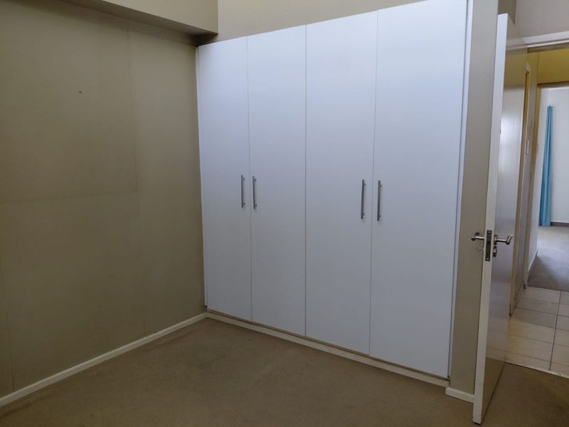 A bedroom featuring white built-in cupboards and neutral wall tones, offering a clean and functional space ready for personalization.