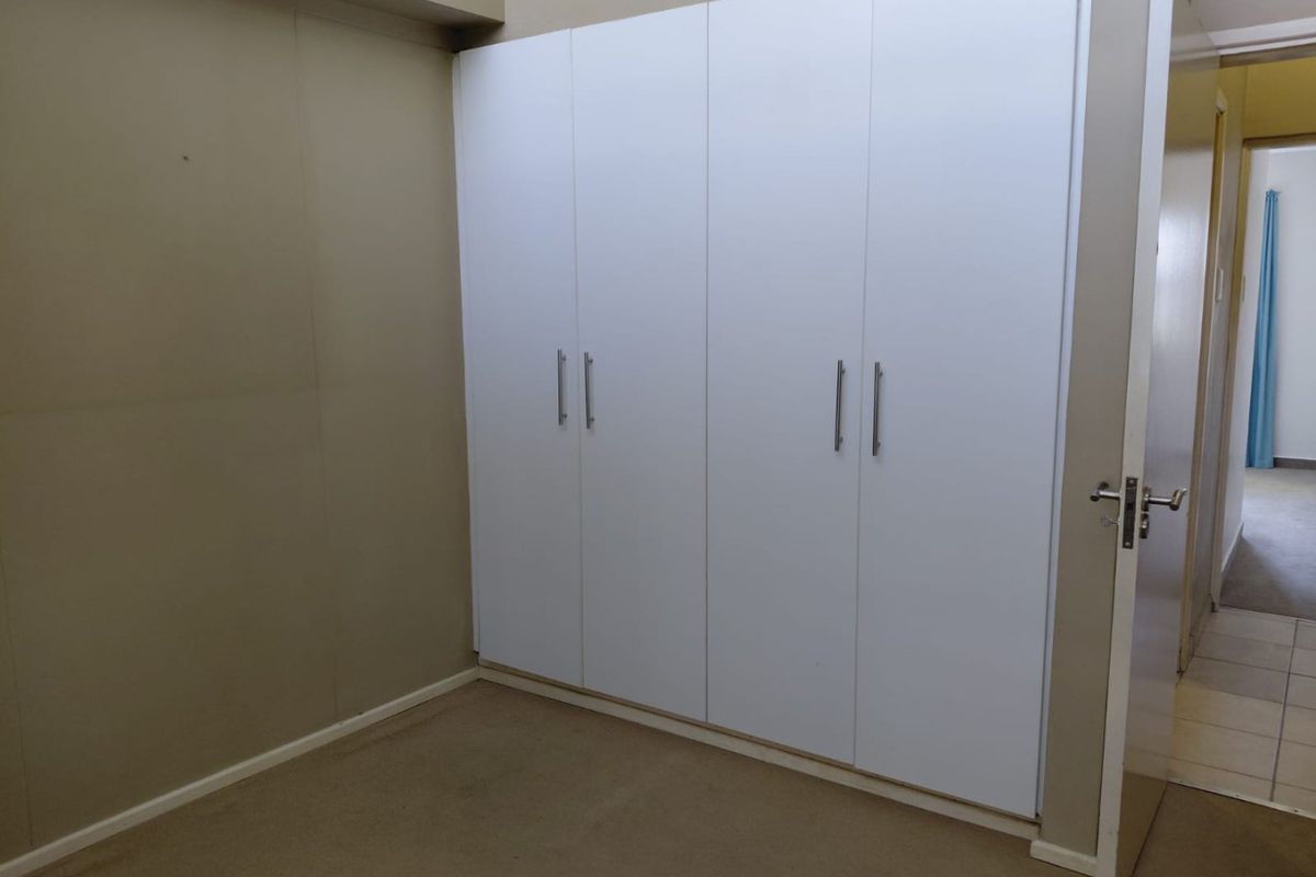 A bedroom featuring white built-in cupboards and neutral wall tones, offering a clean and functional space ready for personalization.