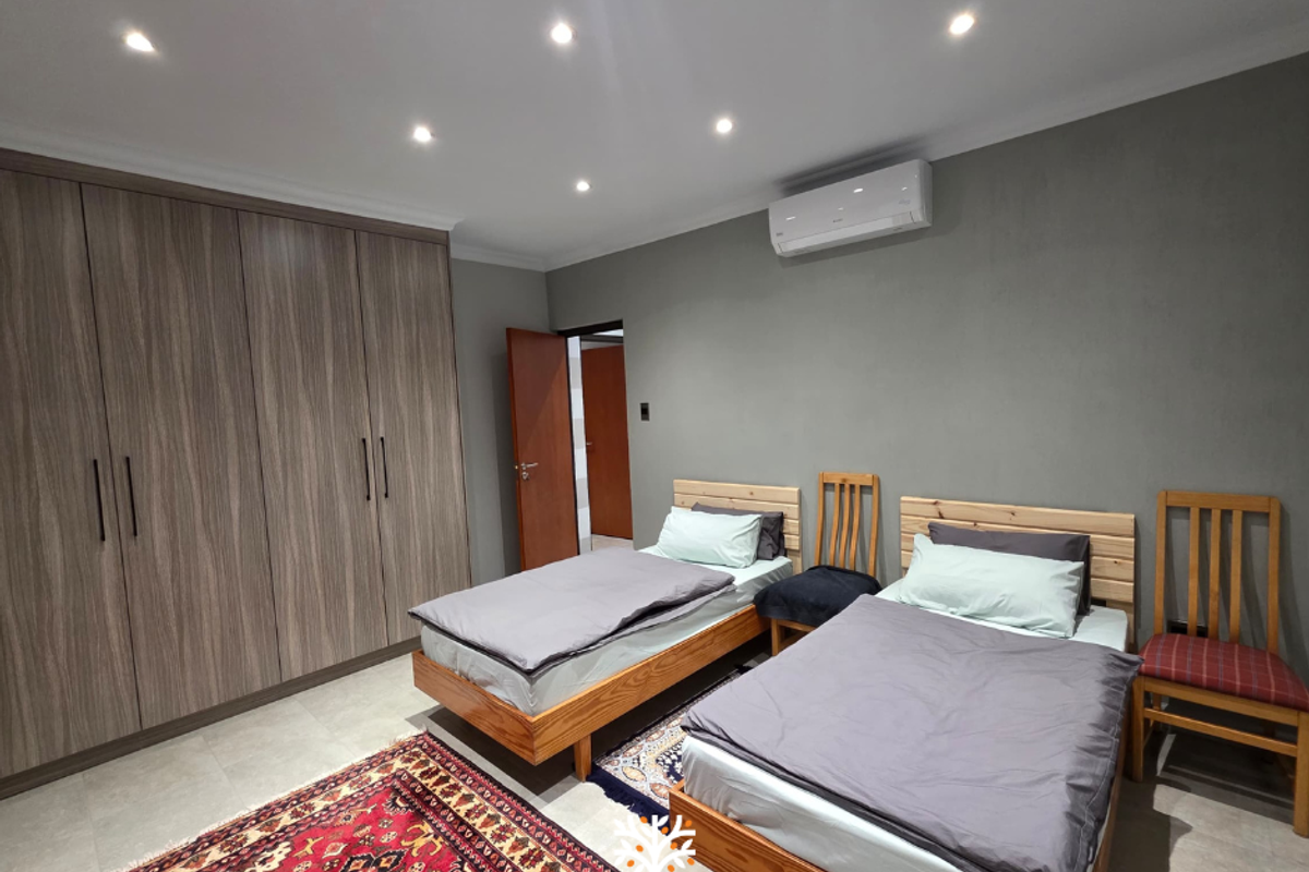 A well-maintained bedroom featuring built-in wood-grain wardrobes, recessed ceiling lighting, and a wall-mounted air conditioning unit.