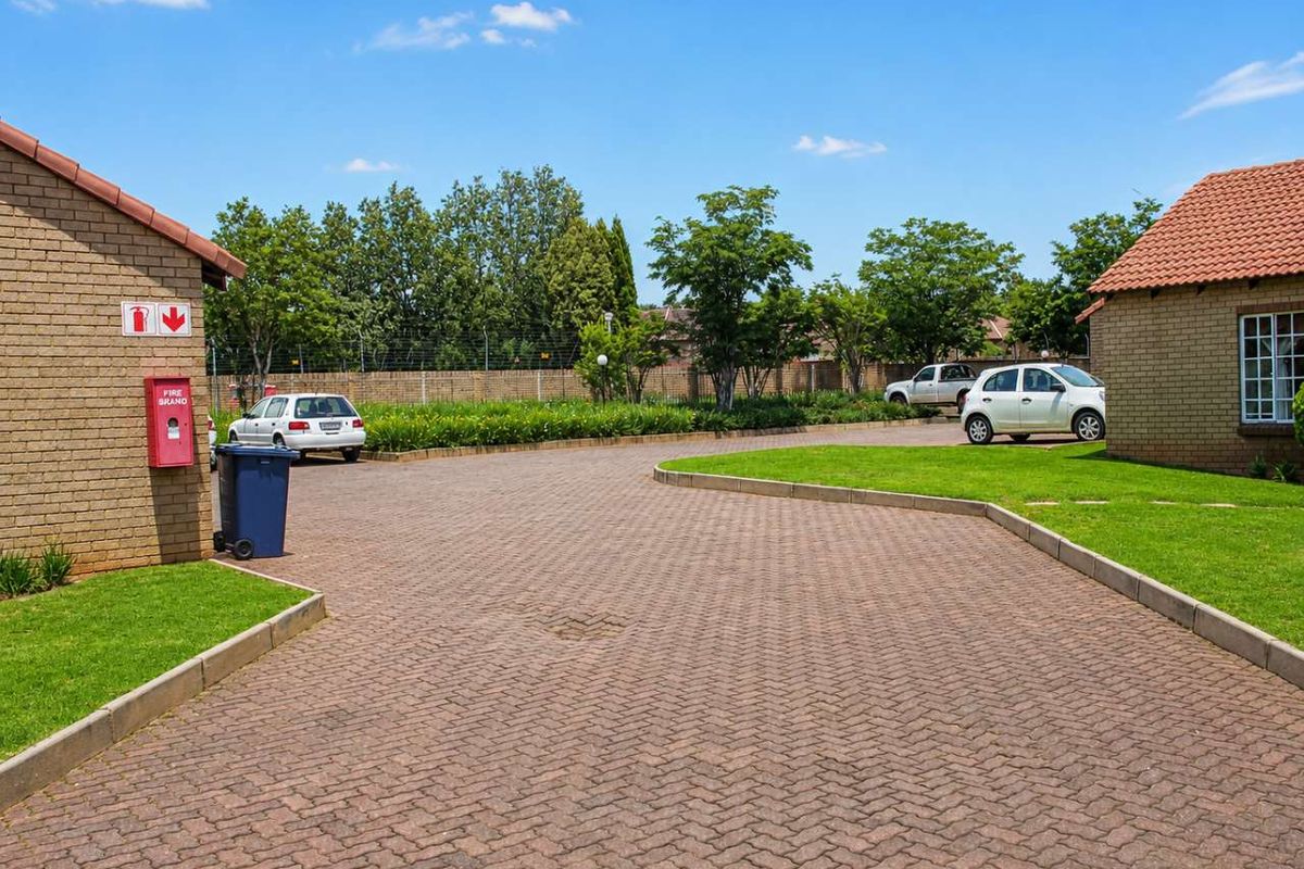 A view of the paved driveway and landscaped lawn area within the townhouse complex, featuring brick facade buildings and perimeter fencing.