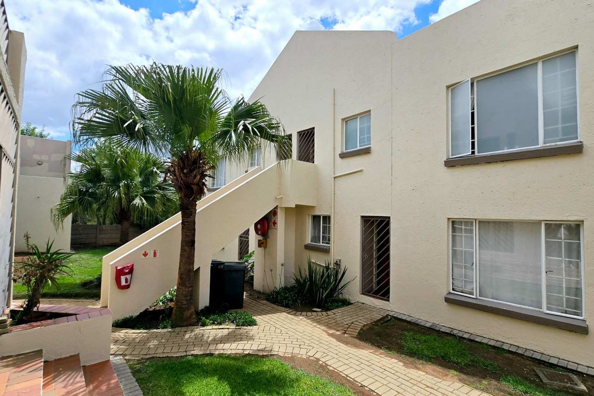 Exterior view of an apartment complex featuring a paved walkway, external staircase, and landscaped garden area.