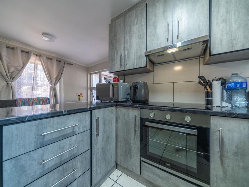 Modern kitchen featuring grey textured cabinetry, stone countertops, built-in oven, electric hob, and extractor fan with a clean tiled backsplash.
