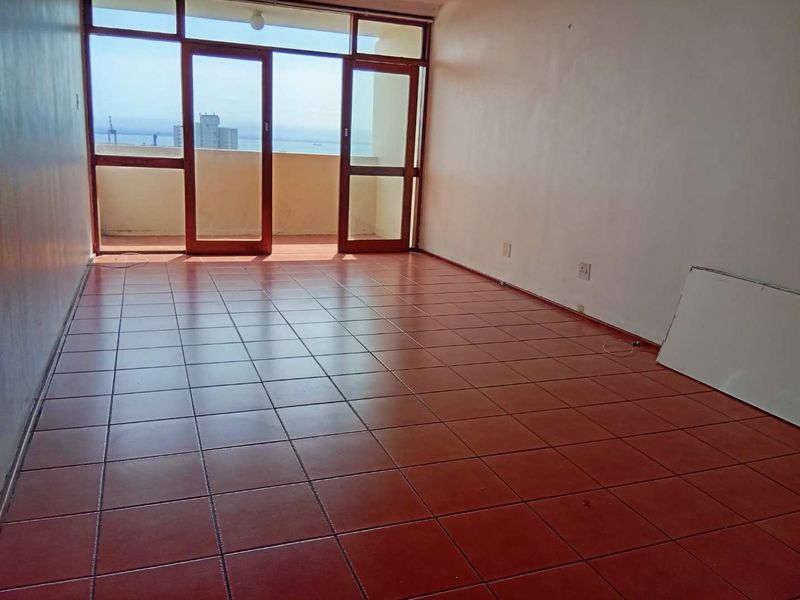 An empty living room featuring terracotta floor tiles and large timber-framed glass doors leading to a balcony with coastal views.