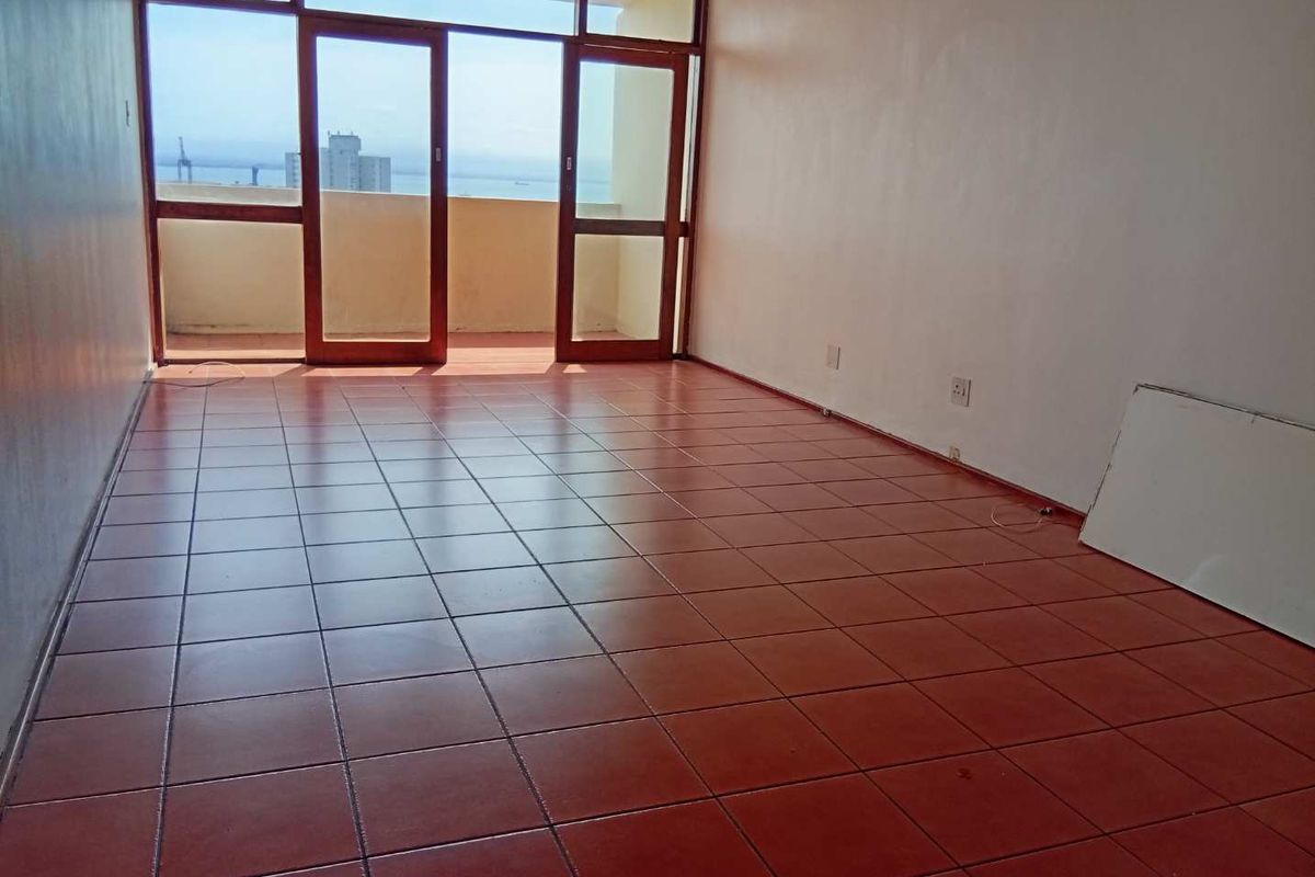 An empty living room featuring terracotta floor tiles and large timber-framed glass doors leading to a balcony with coastal views.