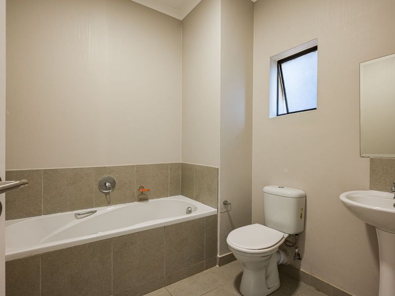 A clean and functional bathroom featuring a bathtub, pedestal basin, and toilet with neutral wall and floor tiling.