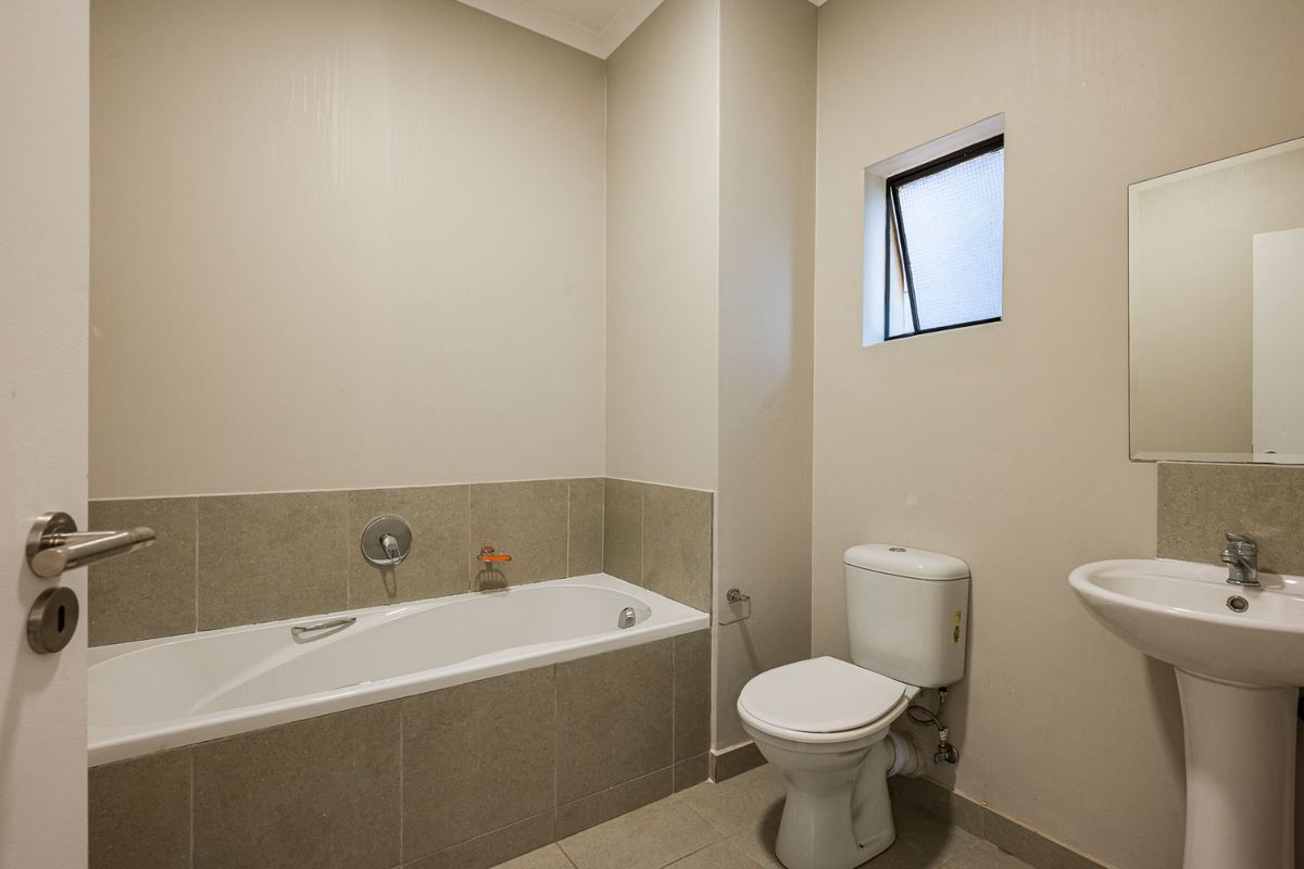 A clean and functional bathroom featuring a bathtub, pedestal basin, and toilet with neutral wall and floor tiling.