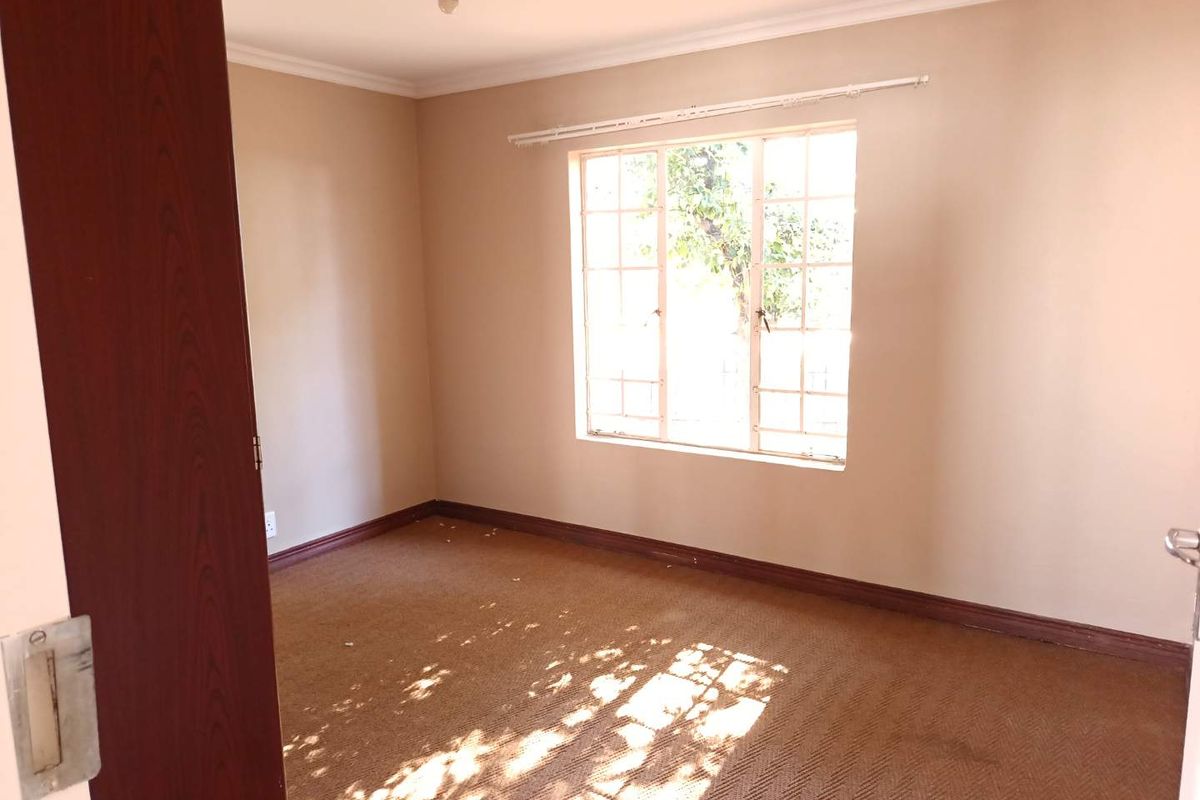 An empty bedroom featuring carpet flooring, a steel-framed window, and a built-in cupboard, offering a blank canvas for potential updates.