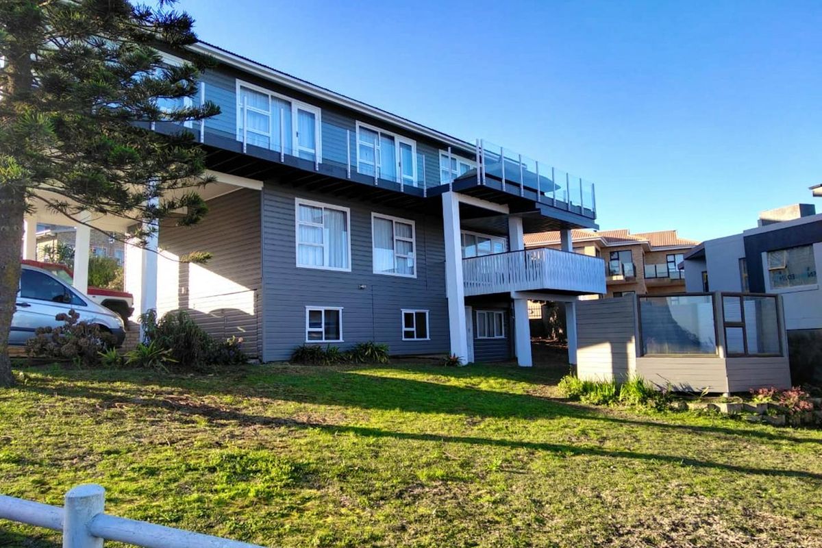 Rear view of a multi-level house featuring weatherboard cladding, a raised balcony with a glass balustrade, and a timber deck overlooking the garden.