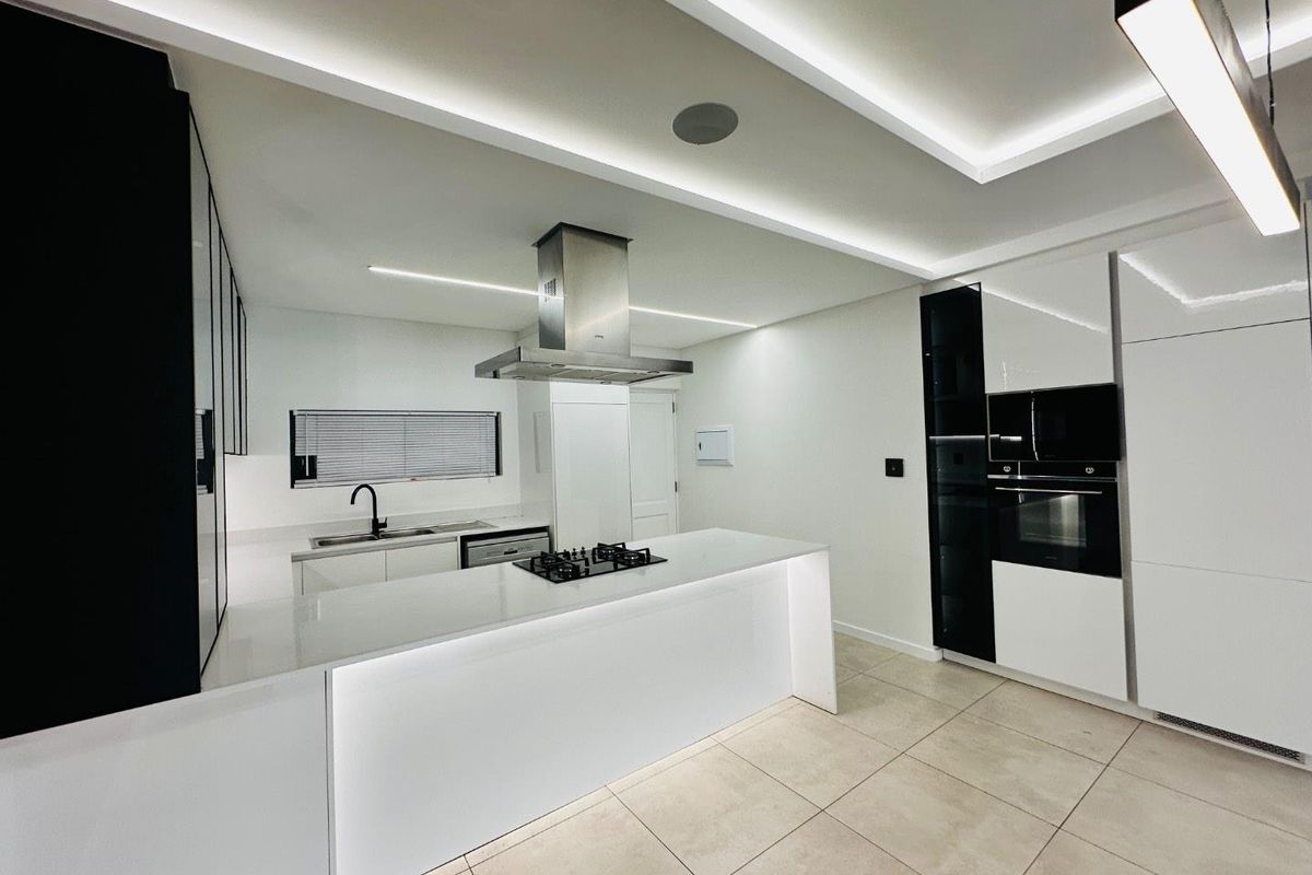 Modern, high-end kitchen featuring a central island with gas hob, integrated appliances, sleek high-gloss cabinetry, and sophisticated recessed LED lighting throughout.