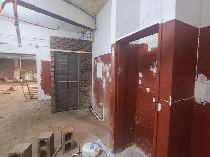 An industrial utility space featuring exposed fire sprinkler piping, concrete flooring, and unfinished wall surfaces, suitable for renovation or industrial repurposing.