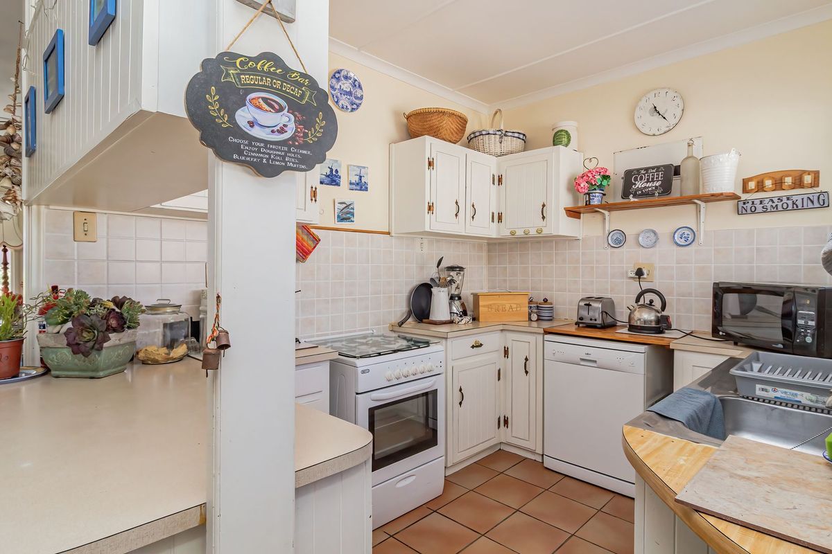 A functional kitchen featuring white cabinetry, tiled backsplash, a freestanding stove, and a stainless steel sink with tiled flooring.