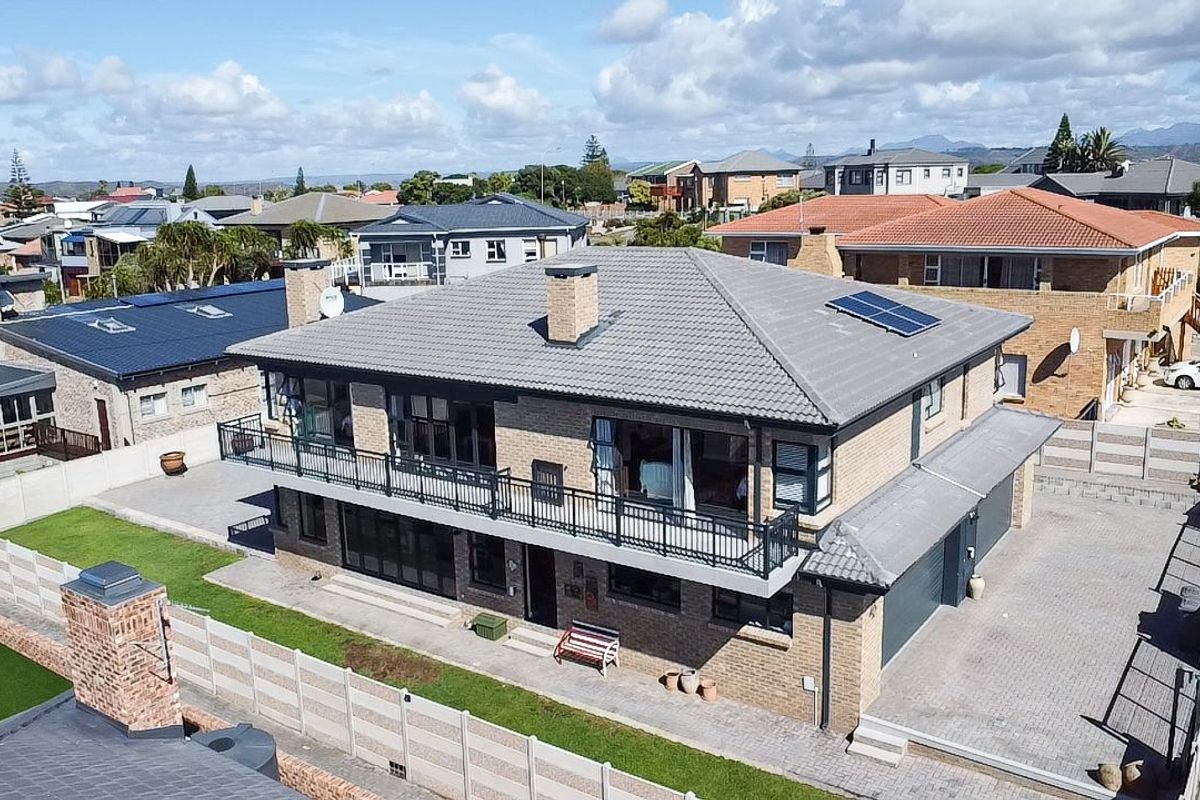 Aerial view of a two-story brick house featuring a tiled roof with solar panels, a balcony with metal railings, and a paved driveway.