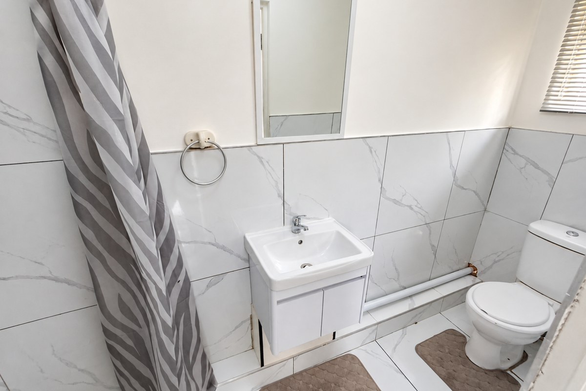 A compact bathroom featuring marble-look wall and floor tiles, a modern vanity with basin, and a standard toilet.