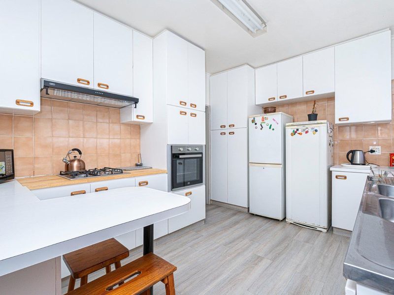 A functional kitchen featuring white cabinetry, a gas hob, built-in oven, tiled backsplash, and a double sink with laminate flooring.