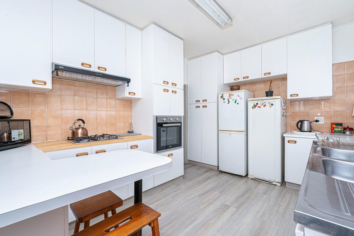 A functional kitchen featuring white cabinetry, a gas hob, built-in oven, tiled backsplash, and a double sink with laminate flooring.
