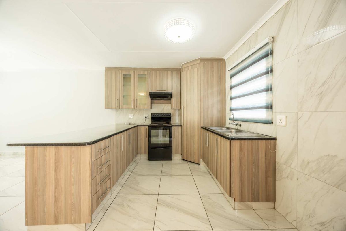 A clean and functional kitchen featuring wood-finish cabinetry, granite countertops, tiled flooring, and integrated appliances, offering a bright and well-maintained workspace.
