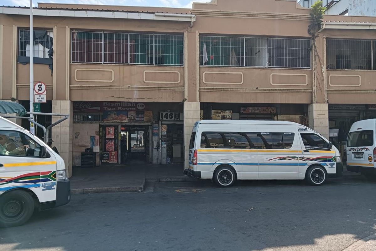 Street-level view of a commercial building facade featuring storefronts with security bars and weathered concrete exterior.