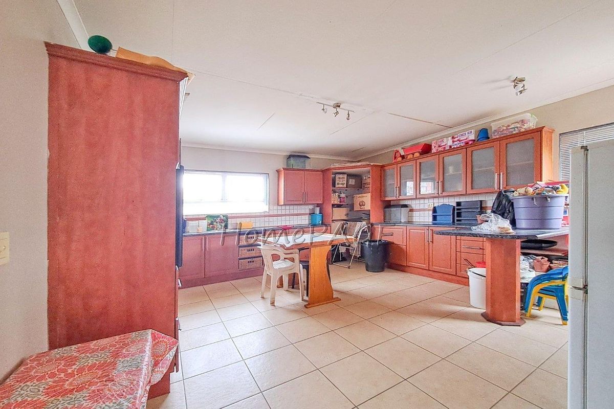 Spacious kitchen featuring extensive wooden cabinetry, tiled flooring, and a central breakfast bar area, offering ample storage and workspace potential.