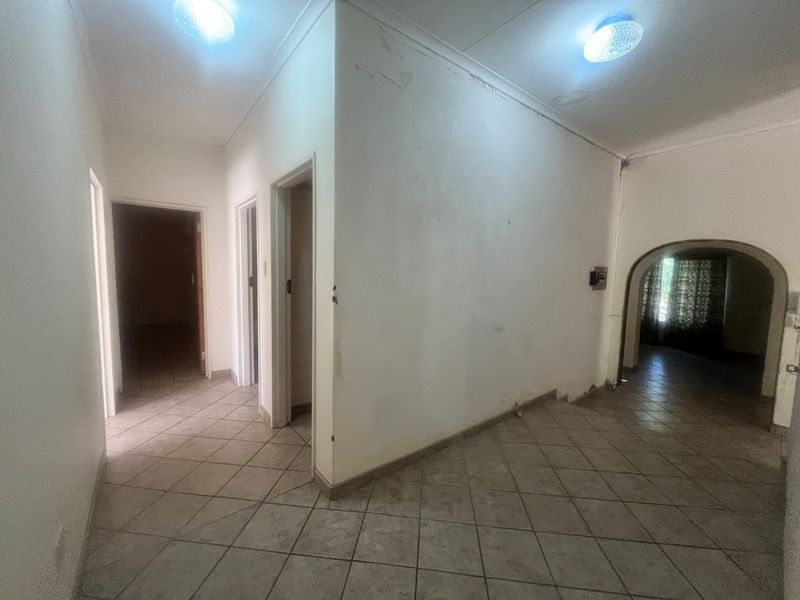 A spacious, empty hallway featuring tiled flooring, arched transitions, and ceiling lighting, currently requiring cosmetic updates to the wall finishes.