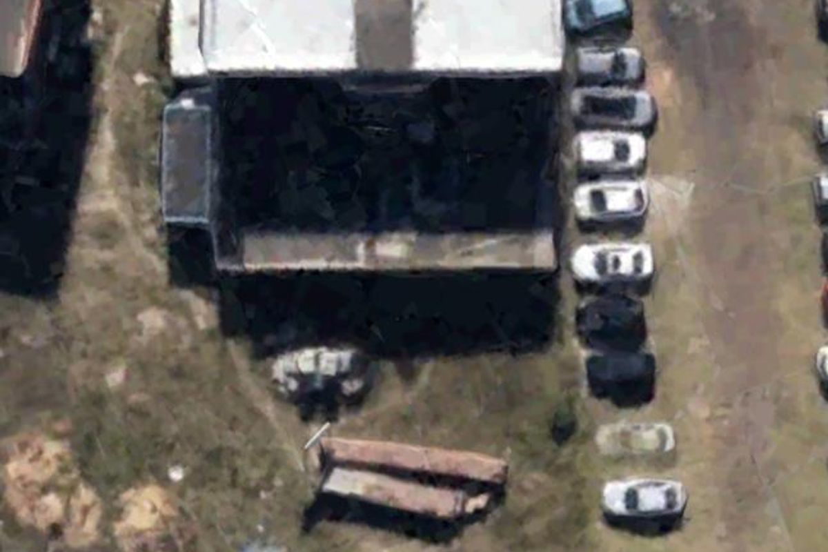Aerial view of an industrial property featuring a flat-roofed building, surrounding parking area, and adjacent open land.