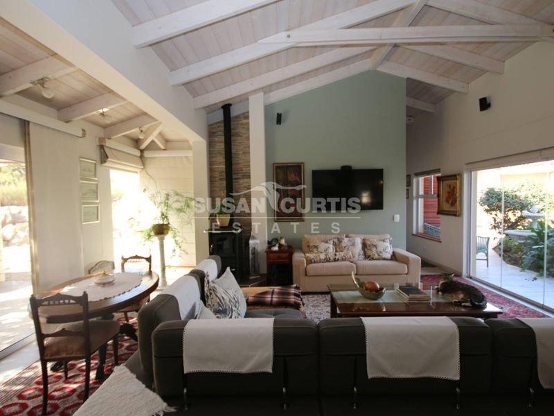 Spacious open-plan living area featuring a vaulted timber ceiling, exposed rafters, and a prominent stone-surround freestanding fireplace with large sliding glass doors.