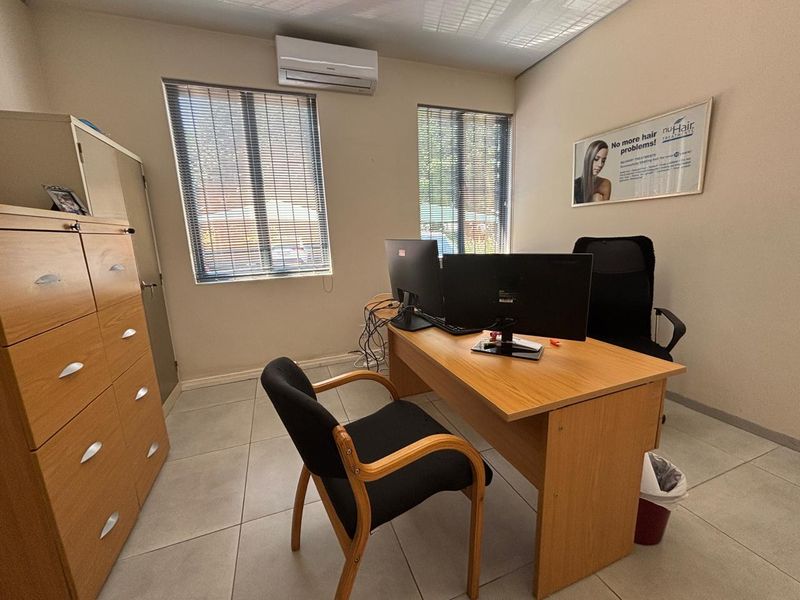 A functional office space featuring tiled flooring, venetian blinds, and a wall-mounted air conditioning unit.