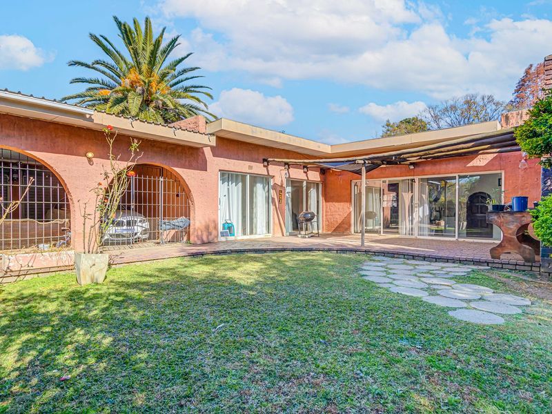 Rear view of the property featuring a paved patio area, arched architectural details, sliding glass doors, and a garden space.