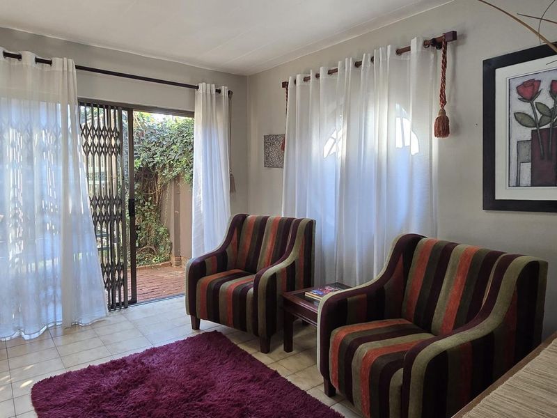 A living room featuring tiled flooring and a sliding glass door with a security gate, providing direct access to the outdoor patio area.