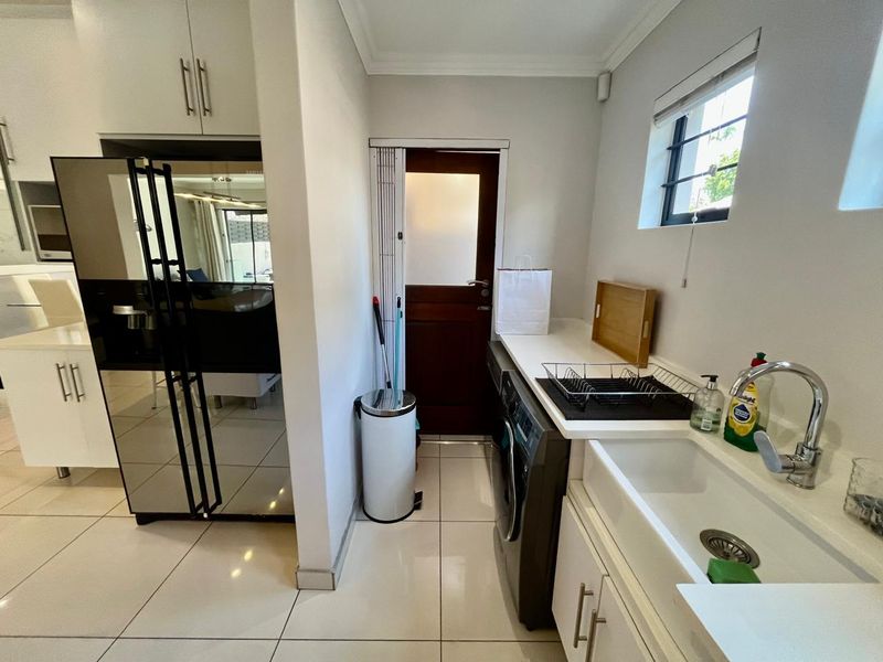 A functional scullery area featuring built-in cabinetry, an undermount sink with a modern mixer tap, and tiled flooring with direct access to the exterior.