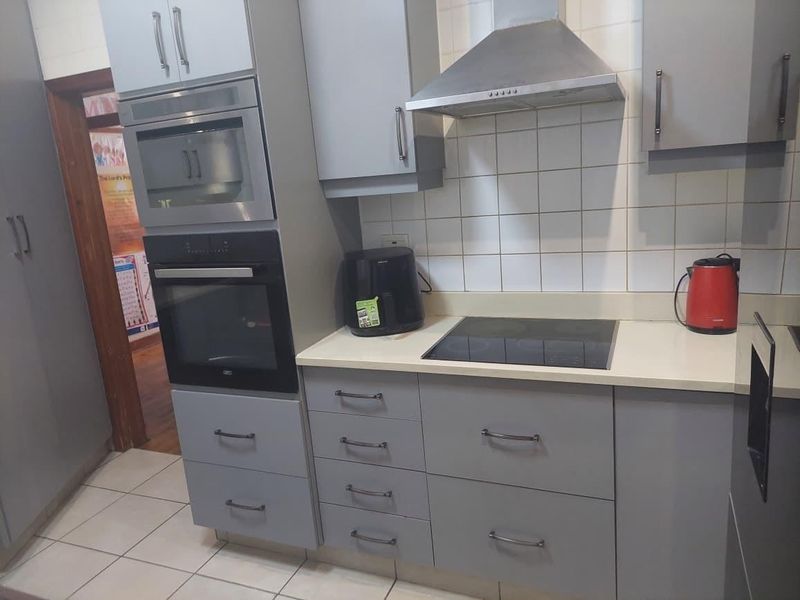 A modern kitchen featuring grey cabinetry, built-in oven and microwave, electric hob with extractor fan, and tiled splashback.