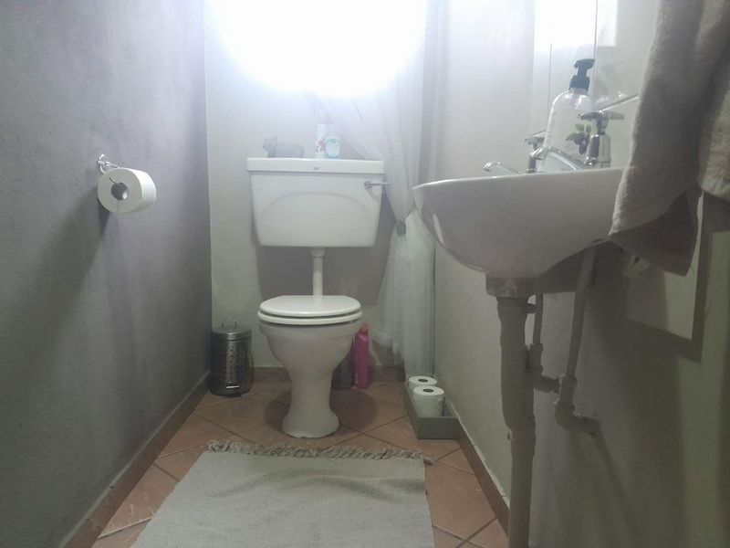 A compact bathroom featuring a standard toilet and pedestal basin with tiled flooring and exposed plumbing.