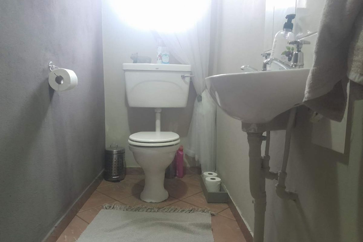 A compact bathroom featuring a standard toilet and pedestal basin with tiled flooring and exposed plumbing.