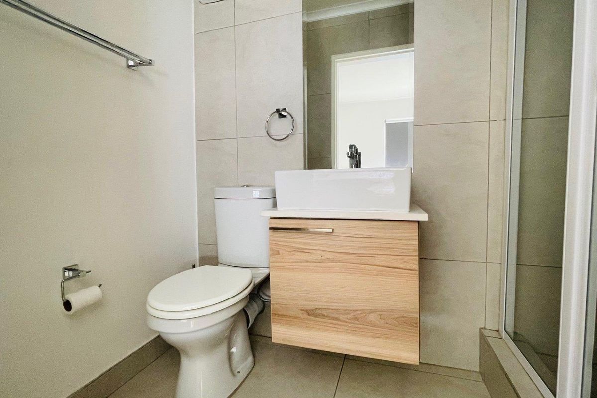 Modern bathroom featuring a wall-mounted wooden vanity with a vessel sink, a toilet, and a glass-enclosed shower with neutral wall tiling.