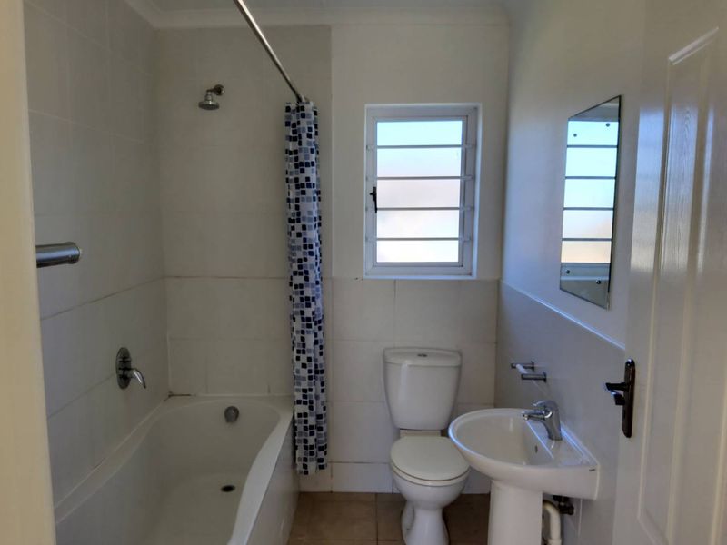 A functional bathroom featuring a bathtub with shower, pedestal sink, and toilet, finished with neutral wall and floor tiles.