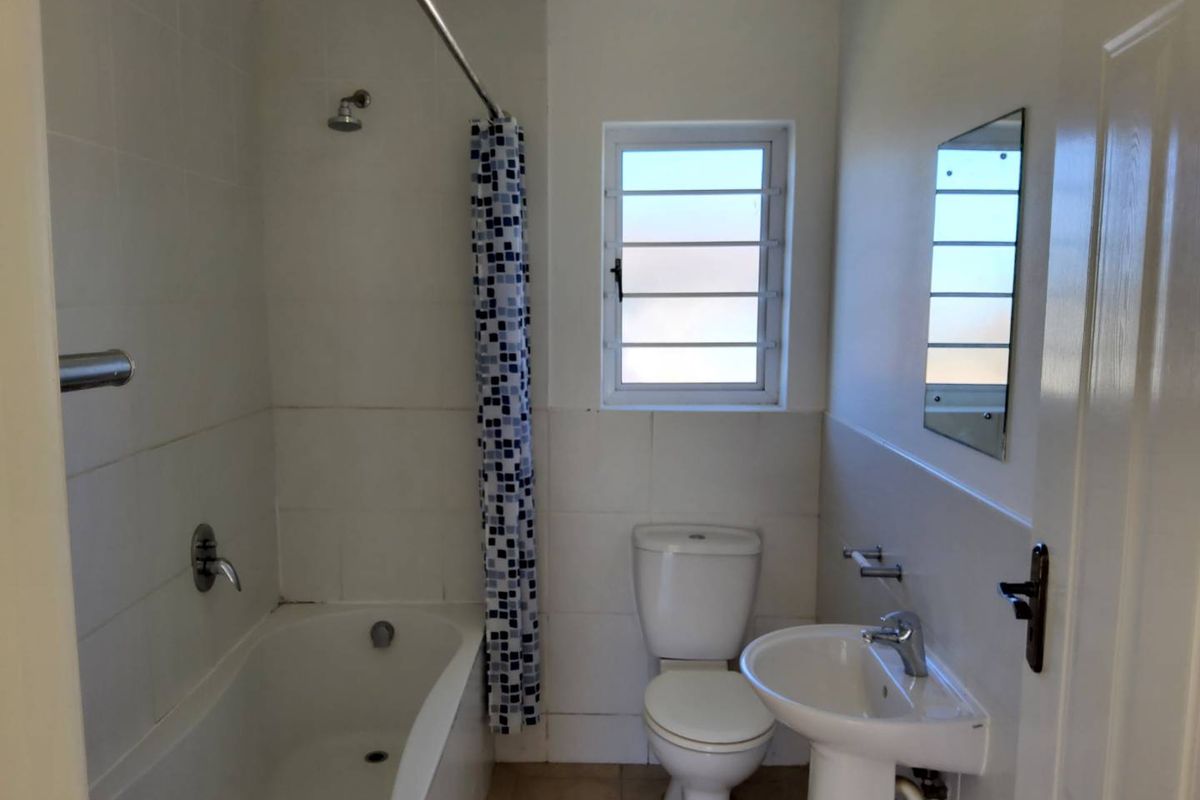 A functional bathroom featuring a bathtub with shower, pedestal sink, and toilet, finished with neutral wall and floor tiles.