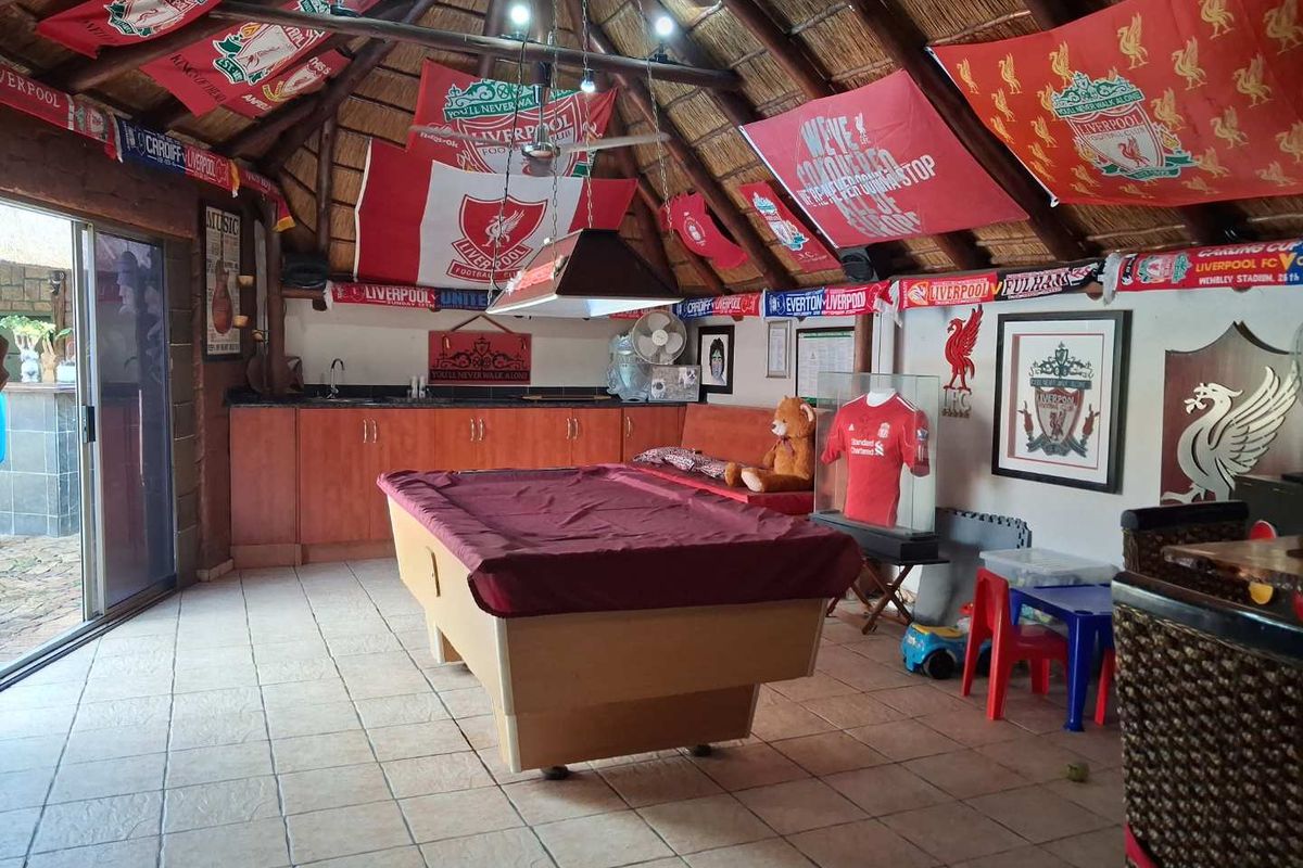Spacious entertainment area featuring a thatched roof, tiled flooring, built-in bar cabinetry with sink, and sliding door access to the patio.