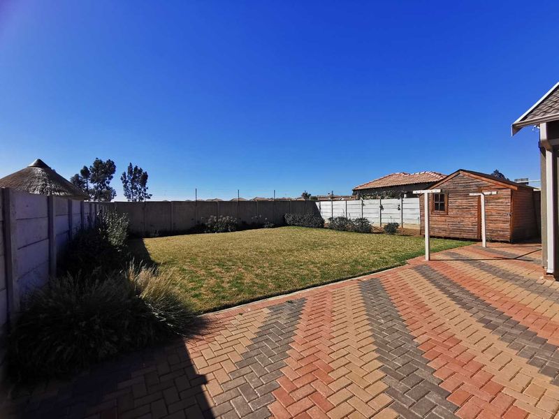 A well-maintained rear garden featuring a paved patio area, a neat lawn, and a wooden storage shed enclosed by precast concrete walls.
