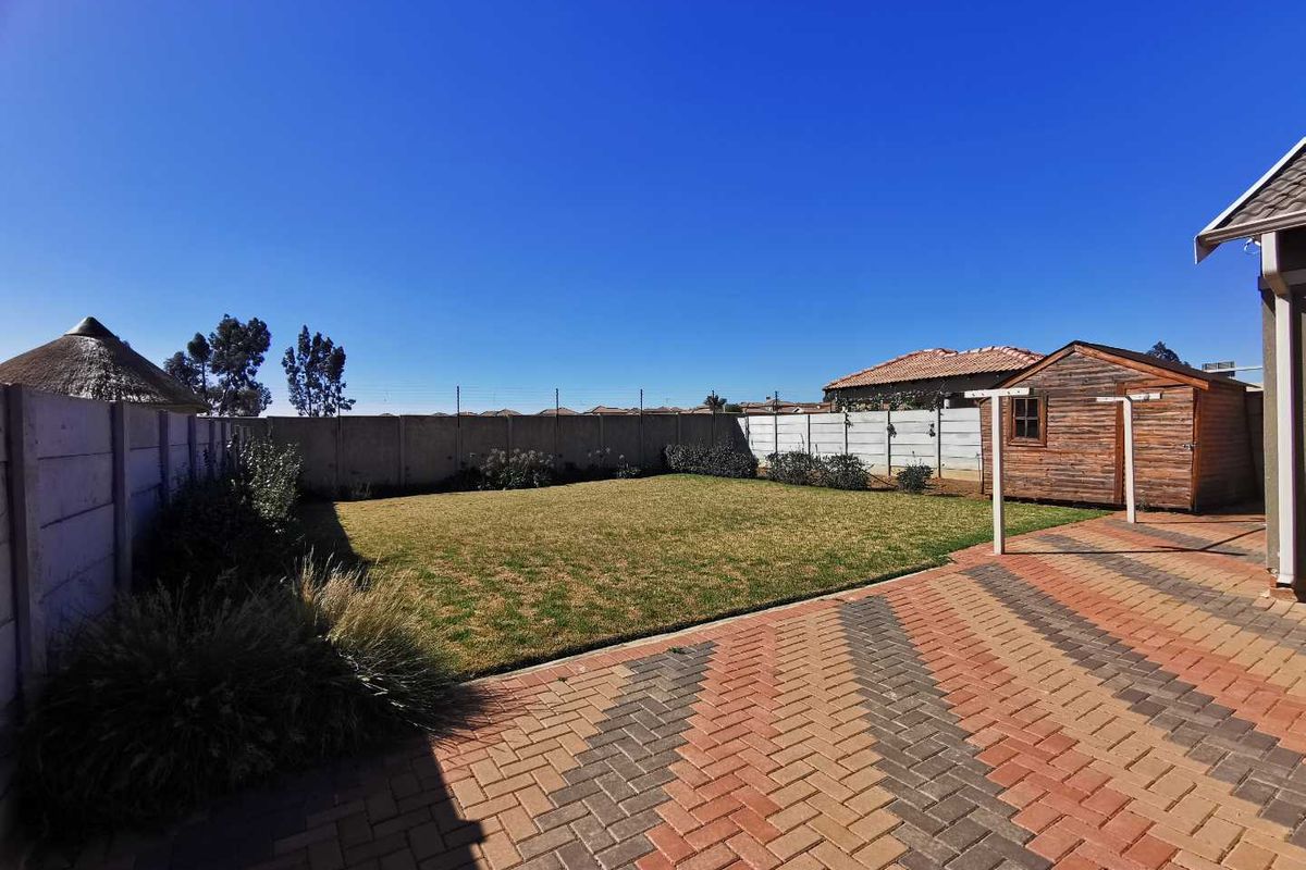 A well-maintained rear garden featuring a paved patio area, a neat lawn, and a wooden storage shed enclosed by precast concrete walls.