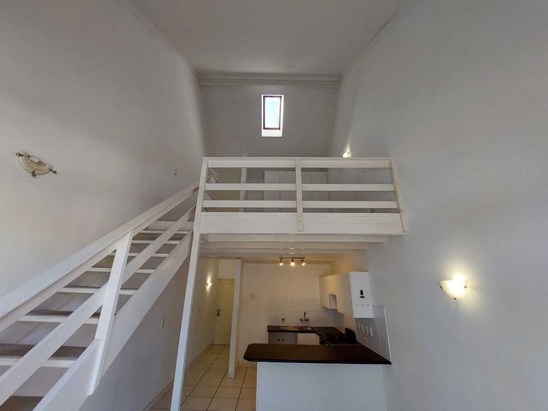 Open-plan apartment interior featuring a mezzanine level, timber staircase, and a functional kitchen area with tiled flooring and a skylight.