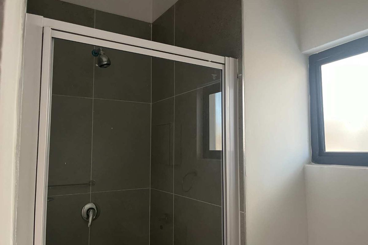 A clean bathroom shower area featuring grey wall tiles, a white framed shower enclosure, and a window for natural light.