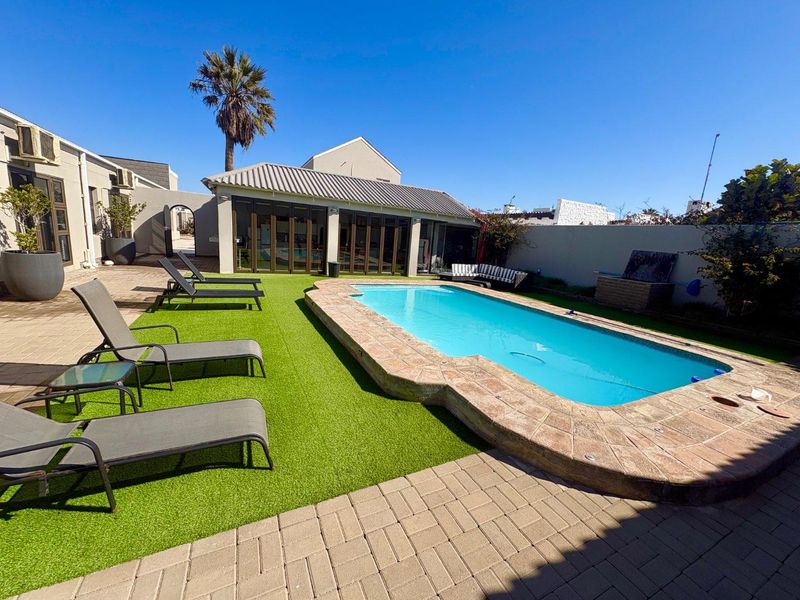 Outdoor pool area featuring a swimming pool with stone coping, artificial turf, paved patio space, and access to the main dwelling via stacking doors.