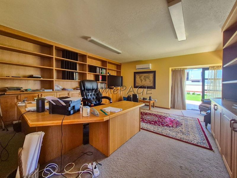Spacious home office featuring extensive built-in wooden shelving, cabinetry, and direct access to the garden through a sliding glass door.