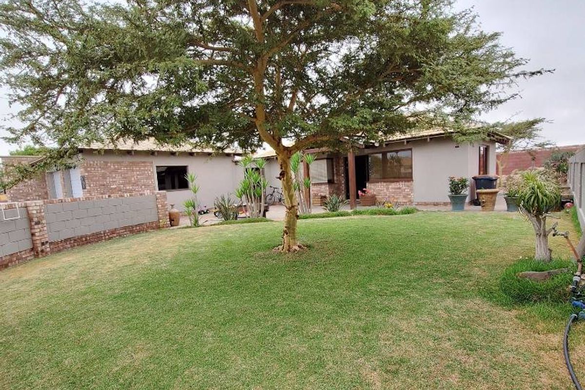 A spacious rear garden featuring a well-maintained lawn, a mature central tree, and brick boundary walls, providing a private outdoor area.